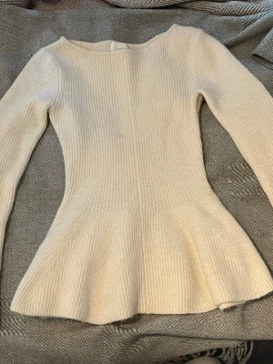 Krämvit peplumstickad tröja H&M - Säljer en krämvit stickad tröja från H&M i storlek XS. Tröjan har en figurnära passform med peplumvolang nedtill, rund halsringning och långa ärmar. Ribbstickad struktur i mjukt material, perfekt för en trendig och bekväm look.