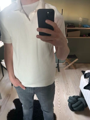Vit ribbad piké med krage - Säljer en stilren vit piké med ribbad struktur och klassisk krage. Skjortan har korta ärmar och en relaxed fit som passar perfekt till jeans eller shorts. Tillverkad i mjukt material för skön känsla hela dagen. 