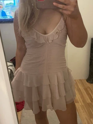 Ljusrosa volangklänning med v-ringning - Supersöt ljusrosa kortklänning med v-ringning och volangdetaljer både vid urringningen och längs kjolen. Klänningen är ärmlös och har en feminin, flowy passform som känns både romantisk och trendig. Perfekt för sommarens alla tillfällen.