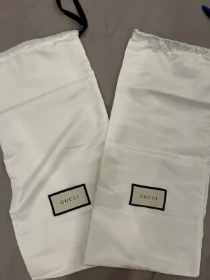Svarta sandaler med klack från Gucci - Snygga svarta sandaler från Gucci med bred rem i skinn och ikonisk GG-logga i guld framtill. Skon har öppen tå och hög blockklack för en trendig look. Medföljer original dustbags från Gucci.