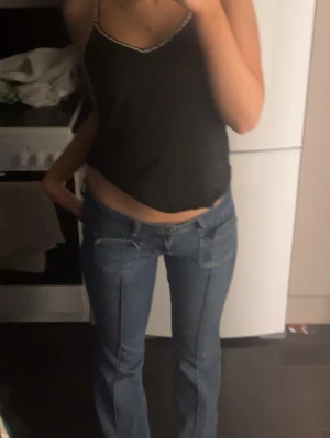 Blå bootcut jeans med fickdetaljer - Säljer ett par blå bootcut jeans med låg midja och snygga fickdetaljer fram. Jeansen har en klassisk femficksmodell och är i ett mjukt denimtyg som sitter skönt. Perfekta för en avslappnad och trendig look.