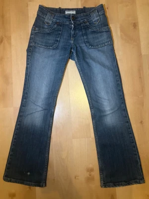 Blå bootcut jeans från Lee - Säljer ett ytterligare par super fina låg midjade bootcut jeans från Lee, men coola detaljer och klassiska knappar på bakfickorna.  Storlek: W30 L31 Inre benlängd: 73 cm Midjemått rakt över: 36 cm Jag är 170 cm och de var lite korta på mig, ’men de passar säkert bra på någon mellan 160-166. Jeansen är i väldigt gott skick, och ser ut att ha använts få gånger! Det finns ett mycket litet slitage vid det vänstra byxbenet, och även vid byxans slut. Jeansen är insydda sen tidigare, går att sprätta up