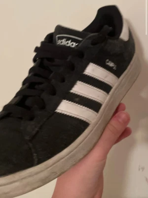 Adidas Campus svarta sneakers - Svarta Adidas Campus sneakers med klassiska vita ränder på sidorna och vit hälkappa med logga. Ovandel i mocka och platt vit sula. Snygg och tidlös modell som passar till det mesta. Skon har svarta skosnören och Campus-tryck på sidan.
