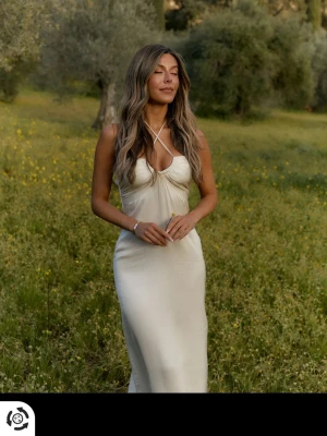 Avora klänning - Säljer en elegant creamfärgad långklänning från Avora med halterneck och snygg knytning i halsen. Helt oanvänd då den är för liten för mig!!  Har legat i min garderob i ett år därav den ser såpass skrynklig ut! 