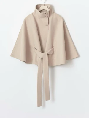 Slutsåld Gina poncho kappa  - Snygg beige cape-kappa med hög krage, knappar framtill och ett brett knytskärp i midjan. Kappan har vida ärmar och är tillverkad i ett mjukt material som ger en elegant look. Perfekt för dig som vill ha något stilrent och trendigt.