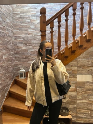 Beige teddyjacka med dragkedja - Mysig beige teddyjacka med rak passform och dragkedja framtill. Jackan har två sidofickor och ribbad nederkant. Perfekt för att hålla sig varm och snygg under kyliga dagar. Materialet är fluffigt och mjukt, vilket ger en trendig look.