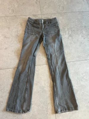 Grå bootcut jeans med sömdetaljer ifrån Gina young  - Säljer dessa grå jeans i storlek 164 ifrån Gina Young med markerade sömmar längs benen. Jeansen har framfickor med extra sömdetaljer och klassiska bakfickor. Använda vid ett tillfälle så som nya.