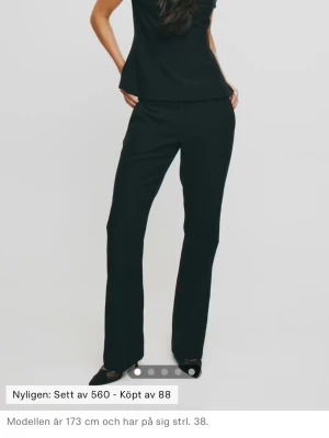 Svarta Lågmidjade kostymbyxor med raka ben - Stilrena svarta kostymbyxor med raka ben och pressveck. Byxorna har normal midja och diskreta fickor i sidorna. Perfekta för en clean och klassisk look. Materialet ser ut att vara en mjuk och följsam vävd kvalitet.