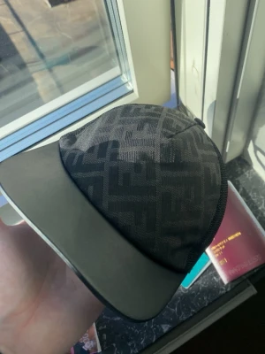 Svart Fendi keps med FF-mönster - Säljer en svart keps från Fendi med det klassiska FF-logomönstret över hela kepsen. Skärmen är i svart material och kepsen har en modern, stilren form. Perfekt för dig som vill ha en exklusiv och trendig accessoar.