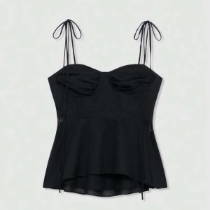 Svart topp  - Supersnygg svart topp med tunna axelband som knyts i rosetter. Toppen har markerad byst och lätt utsvängd nederdel. Helt oanvänd. I storlek M men är ganska liten i storleken över bysten. 