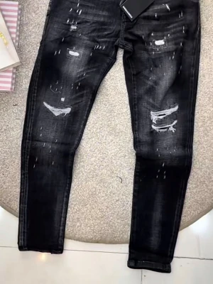Svarta slitna jeans från Dsquared2 - Säljer ett par svarta jeans från Dsquared2 med distressed detaljer och slitningar på både lår och knän. Jeansen har en smal passform och klassisk femficksdesign. Materialet är denim med stretch för extra komfort. Perfekta för en trendig och avslappnad look.