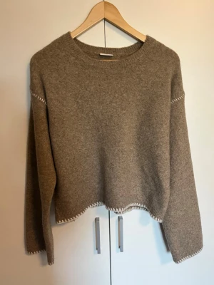 Beige stickad tröja med dekorativa sömmar - Mysig beige stickad tröja från KappAhl. Tröjan är i barnstorlek 170 cm, vilket motsvarar storlek XS. Den har dekorativa vita sömmar vid ärmslut och nederkant samt en rak, något kortare passform. En perfekt stickad tröja för våren. Tröjan är oanvänd. 🫶🫶