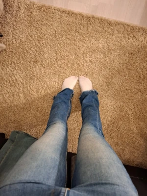 Blå bootcut jeans med rå kant - Säljer ett par blå bootcut jeans med slitning i benslut. Jeansen har klassisk femficksdesign och normal hög midja. 