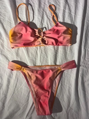 Färgglad bikini i rosa, korall och orange - Snygg bikini med gradient i rosa och orange toner. Överdelen har smala axelband och snygg snörningsdetalj framtill. Perfekt för stranden eller poolen! Använt typ 2 gånger, så som ny!