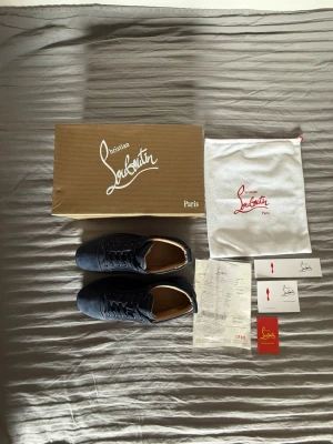 Christian Louboutin skor mörkblå - Snygga mörkblå sneakers från Christian Louboutin i mocka med klassisk röd sula. Lågt skaft och diskret logga på hälen. Skorna har mörkblå skosnören och metallhål för ventilation på sidan. Kommer med originalkartong och dustbag.