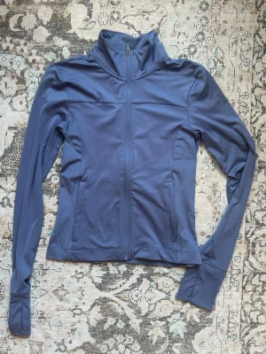 Blå sportjacka med dragkedja - Snygg blå sportjacka med hel dragkedja framtill och hög krage. Jackan har långa ärmar och två sidofickor. Perfekt för träning eller utomhusaktiviteter. Materialet är stretchigt och följsamt.