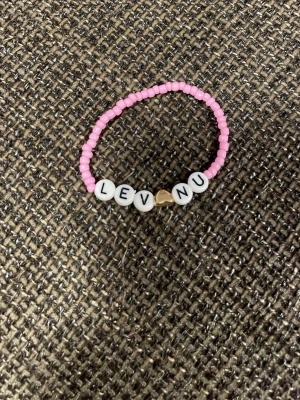 Rosa pärlarmband med text - Sött armband med små rosa pärlor och vita bokstavspärlor som bildar texten 'LEV NU'. Armbandet har även en liten guldfärgad hjärtpärla i mitten. Perfekt accessoar för att sprida positiv energi.