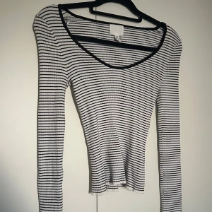 Randig ribbad topp från H&M - Säljer en långärmad, ribbad topp från H&M i svartvitt randigt mönster. Toppen har en urringning och är figurnära med stretchigt material. Perfekt att styla med jeans eller kjol för en enkel men snygg look. 