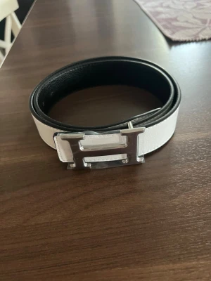 Vitt skärp med ett H - Snyggt vitt skärp, silverfärgat H-spänne. Bältet är 110 passar nästan alla. Skärpet är helt nytt. klassisk design som passar till många outfits. Perfekt accessoar för att lyfta din look.🤩
