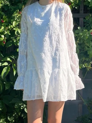 Vit student/ avslutnings klänning  - Säljer min fina och populära klänning med blom-detaljer från NA-KD, endast använd vid 2 tillfällen och därför som i nyskick. Perfekt för dig som ska ta studenten, söker klänning till skolavslutning eller finklänning. Orginalpris på 699kr. Hör gärna av dig vid frågor!