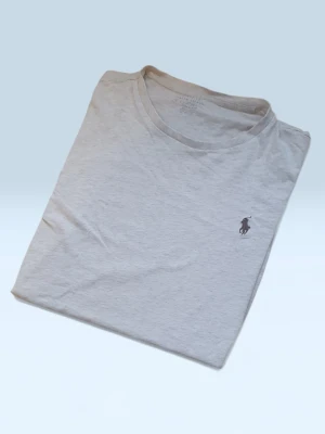 Ljusgrå t-shirt från Ralph Lauren - Säljer en stilren ljusgrå t-shirt från Ralph Lauren med klassisk rund hals och korta ärmar. T-shirten har den ikoniska lilla polospelaren broderad på bröstet. Tillverkad i mjuk bomull för en skön känsla.