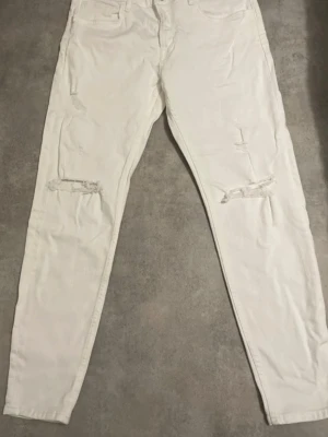 Jeans  - Säljer ett par vita jeans från zara med snygga slitningar på båda benen. Modellen är rak och har klassiska fem fickor samt knappgylf. Perfekta för dig som gillar en trendig och avslappnad stil.