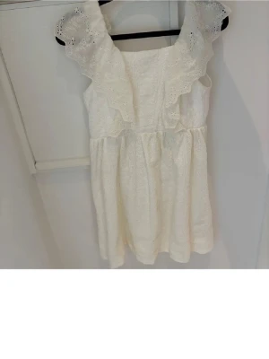 Vit klänning med volang och broderi - Superfin vit klänning med breda volangärmar och broderade detaljer. Klänningen är kort och har en luftig passform.