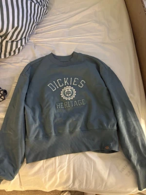 Vintage Dickies sweatshirt - Snygg blå/grön sweatshirt från Dickies Heritage med broderad logga och text framtill. Tröjan har rund halsringning, ribbade muddar vid ärmslut och nederkant samt en avslappnad passform. Perfekt för en casual och street-inspirerad stil.