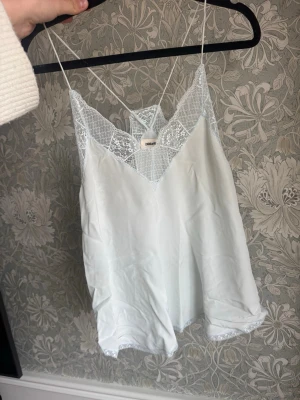 Zadig & Voltaire Linne - Säljer en ljus blått/grönt linne från Zadig med tunna axelband och vackra spetsdetaljer vid urringning och nederkant. Toppen har en v-ringad form och är tillverkad i 100 % silke. Nypris över 1500 kr!