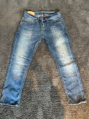 Dondup george jeans - Säljer ett par blå jeans från Dondup med snyggt slitna detaljer och ljusa partier framtill. Klassisk femficksmodell med raka ben och normal midja. Jeansen har en cool tvätt och är tillverkade i bomull för skön känsla.