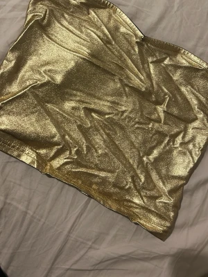 Glittrig guld tubtopp - Snygg glittrig tubtopp i guld som verkligen sticker ut. Perfekt för dig som vill ha något extra till outfiten. Toppens material är glansigt och stretchigt för en bekväm passform. Enkel att matcha med både jeans och kjol.