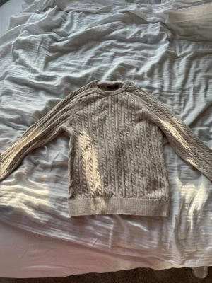 Beige kabelstickad tröja från Next - Snygg beige kabelstickad tröja från Next med rund halsringning och ribbade muddar vid ärmslut och nederkant. Perfekt för lager på lager och enkel att matcha med jeans eller kjol. Klassisk design som funkar året runt. Dock en väldigt liten fläck som knappt snyns på bild 3. Står att den passar för 12 year men den passar mig som 15 åring!!