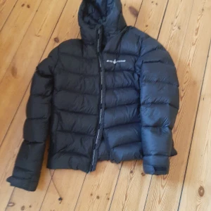 Svart pufferjacka från Everest - Säljer en svart pufferjacka från Sail racing med hög krage och huva. Jackan har quiltad design med breda paneler och dragkedja framtill. Perfekt för kalla vinterdagar och ger ett coolt streetwear-inspirerat uttryck.
