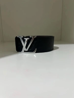Svart bälte i skinn - Snyggt svart bälte i skinn med klassiskt spänne i silver. Bältet har präglade monogramdetaljer längs hela remmen som ger en exklusiv vibe. Perfekt accessoar för att lyfta vilken outfit som helst.