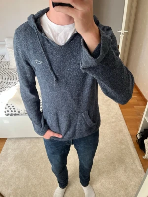 Blå hoodie från Hollister - Stickad blå vintage hoodie från Hollister i storleken M i väldigt skönt material. Hoodien är inte sönder i kragen utan designen är så! 
