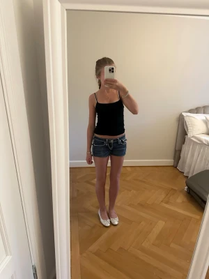 Mörkblå jeansshorts med vita sömmar - Snygga mörkblå jeansshorts med kontrasterande vita sömmar och dekorativa fickor bak. Klassisk femficksmodell med låg midja och bälteshällor. Perfekta för varma dagar och enkel att matcha med olika toppar. Det finns ingen lapp med storlek kvar men de passar mig som är xs/s 