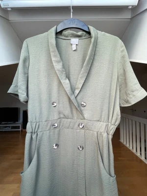 Grön klänning - Snygg grön klänning från ASOS med korta ärmar, dubbelknäppning framtill och två fickor. Avslappnad passform med resår i midjan och mjukt, lätt tyg som ger en skön känsla. 