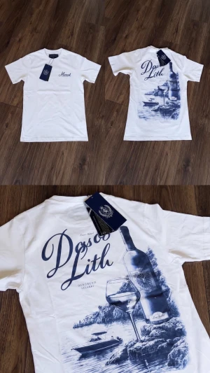 Marcél T-Shirt Vit  -  Vit t-shirt från  Marcél med stort blått tryck på ryggen vinflaska, glas och havsmotiv med texten Dolce Lith. Liten logga på bröstet fram. Klassisk passform, sitter snyggt till jeans eller shorts.