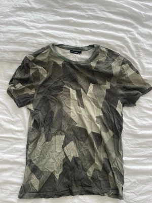 Camouflage t-shirt från J.LINDBERG - Säljer en kortärmad t-shirt från J.LINDBERG med ett  camouflage-mönster i olika nyanser av grön, beige och grå. 