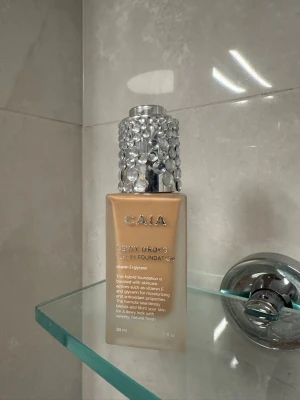 CAIA Dewy Drops Serum Foundation 20W - Foundation från CAIA i nyansen 20W. Kommer i en fyrkantig glasflaska med en silvrig kork dekorerad med stora kristaller. Ger en dewy finish och innehåller vitamin E och glycerin för återfuktning.  Minst 1/3 kvar i flaskan !