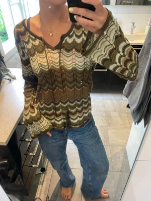 Stickad tunn tröja med mönster - Snygg stickad tunn tröja med vågigt mönster i olika nyanser av grönt, brunt, beige. Tröjan har v-ringning som man kan knyta om man vill. Ärmarna är lite bredare på slutet vilket gör den coolare. Väldigt somrig. Både som en strandtröja eller bara najs tunn att åka båt i/eller ha på kvällar. 