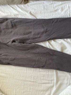 Mörkgrå mjukisbyxor från Gymshark - Mörkgrå mjukisbyxor från Gymshark med dragsko i midjan och diskret logga på vänster sida. Byxorna har smal passform och är tillverkade i ett mjukt och bekvämt material, perfekta för chill eller träning.