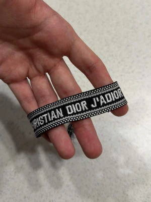 Svart armband - Snyggt svart tygarmband med text i vitt. Armbandet har en bred, vävd design med kontrasterande detaljer och känns både trendigt och exklusivt. Perfekt accessoar för dig som gillar statement-plagg och vill sticka ut.