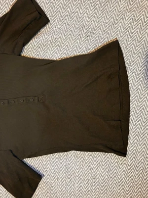 Khaki ribbad topp med knappar - En svart ribbad topp med korta ärmar och knappar framtill. Toppen har en figurnära passform och är gjord i mjukt bomullsmaterial. Enkel och stilren design som passar till många olika looks.