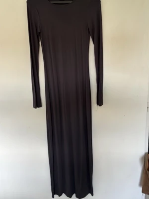 Svart långärmad långklänning - En stilren svart långklänning med rund halsringning och långa ärmar. Klänningen har en rak och enkel siluett som ger ett elegant intryck. Perfekt för dig som gillar minimalistisk stil.