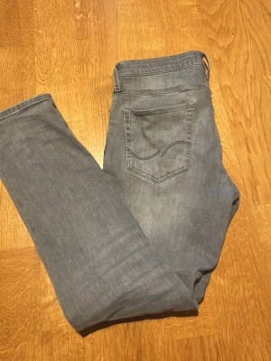 Grå slim fit jeans från Jack and Jones  - Säljer ett par grå slim fit jeans från Jack and Jones. Klassisk femficksmodell med diskret broderad bakficka och normal midja. Jeansen är i mjukt denimtyg och har en snygg tvättad look som passar till det mesta. OBS! Har gjort egna slitningar, se på bilderna.