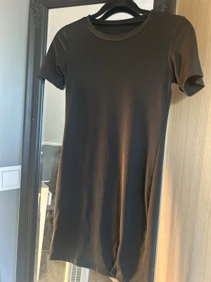 Svart ribbad kortklänning - Säljer en svart ribbad kortklänning med rund hals och korta ärmar. Klänningen har en liten slits nertill på ena sidan.