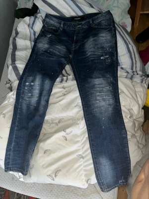 jeans ZAVETTI - Säljer ett par mörkblå jeans från ZAVETTI med snygga slitningar och ljusa tvättade partier. Jeansen har klassisk femficksmodell, orange kontrastsömmar och detaljer som ger en cool, använd look. Perfekta för dig som gillar streetstyle och avslappnad vibe.