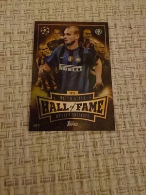 Match Attax Hall of Fame-kort Sneijder - Säljer ett Match Attax Hall of Fame-samlar kort med Wesley Sneijder från Inter. Kortet har svart och guld design med text och klubbmärke, samt Champions League-logga. Materialet är glansigt papper/krom och motivet visar Sneijder i blåsvart matchtröja.