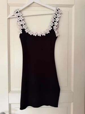 Zara klänning  - Supersöt svart kort klänning med vita 3D-blommor längs axelband och urringning. Helt ny och Säljs ej längre!! Passar både S och XS